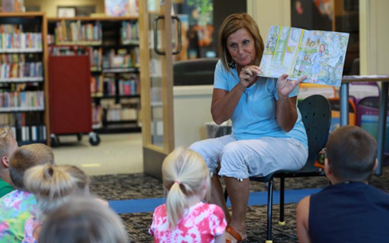 a woman reads a picture book and displays the pages to a group of children in a library
