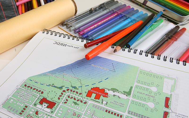 a sketchbook pad with an illustrated map rests next to an open set of markers and pens